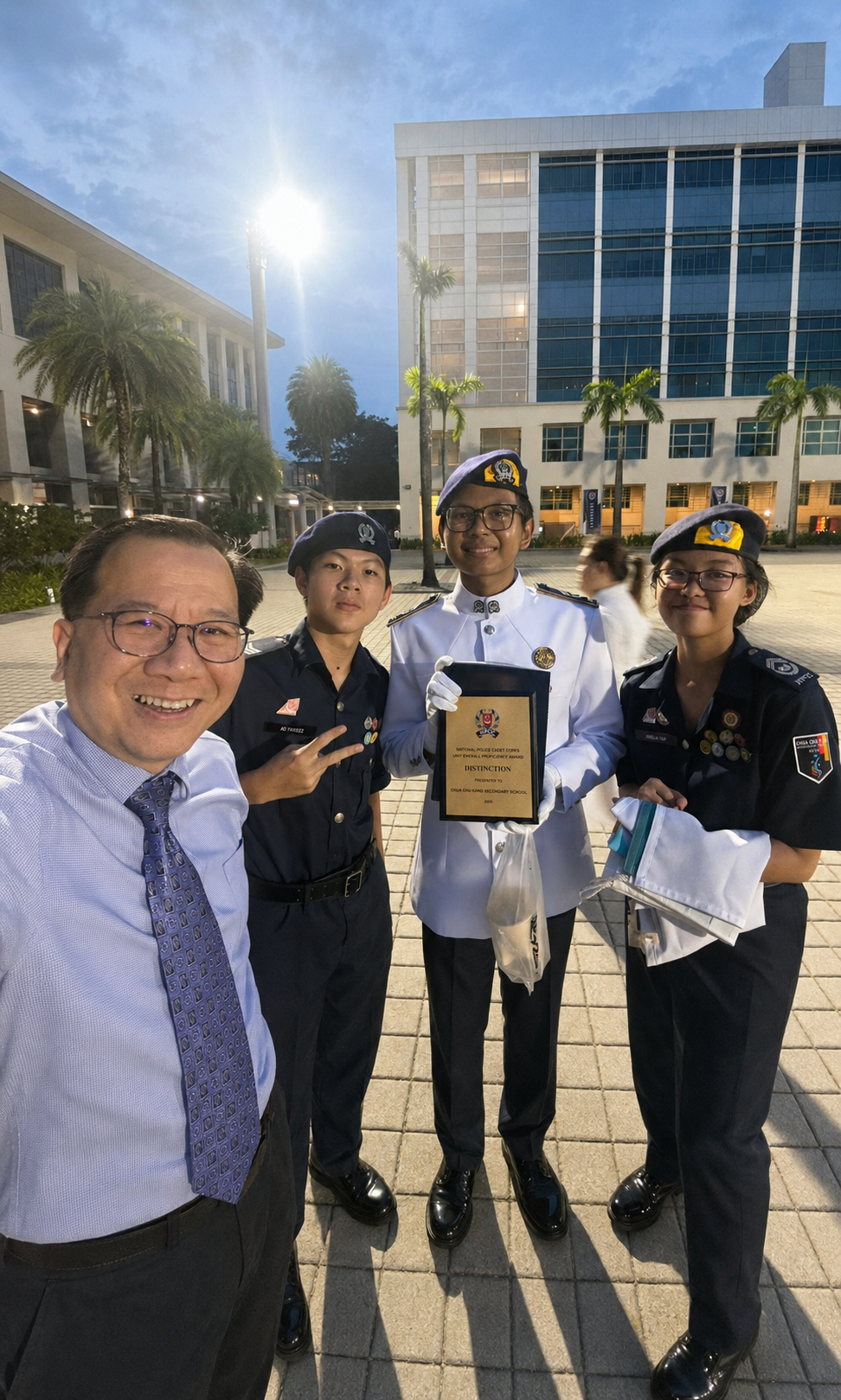 Three NPCC cadets in uniform pose for a selfie with a man; one holds a plaque.